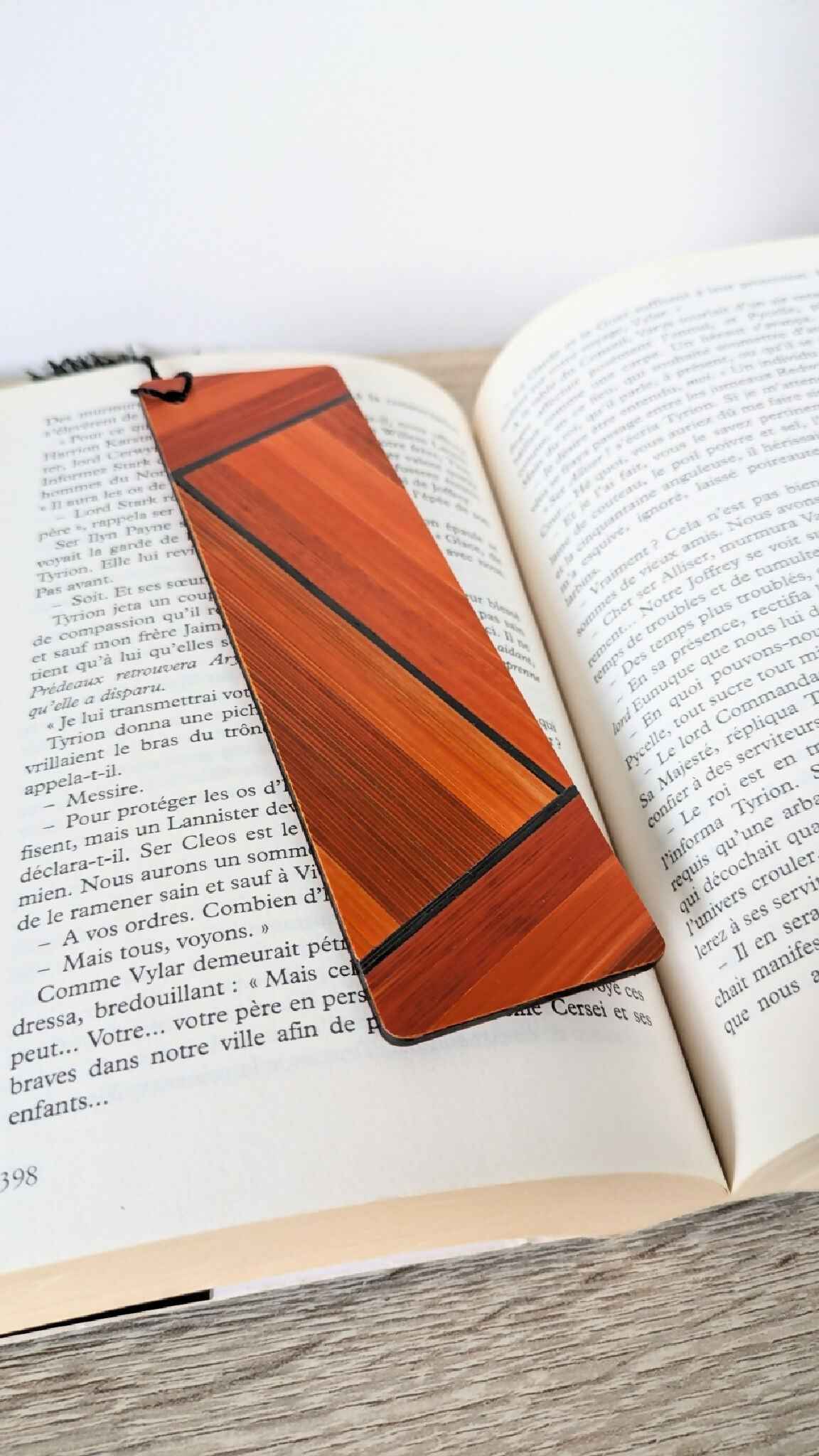 Marque-page en marqueterie de paille orange à lignes, posé sur un livre ouvert