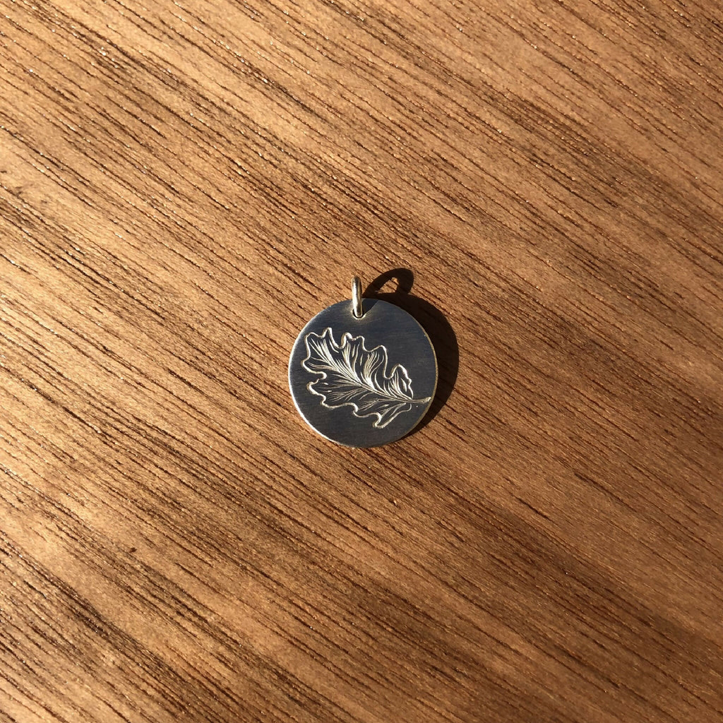 Médaille feuille de chêne en argent 925, forme ronde, bélière visible au sommet.