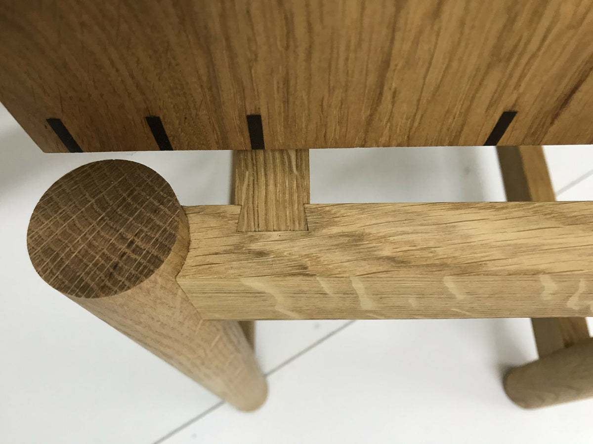 Détail du piètement et de la traverse en chêne, avec pastille ronde de fixation.