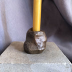 Mini bougeoir en pierre sombre avec bougie jaune, base sur socle.