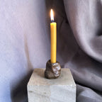 Mini bougeoir en pierre sombre avec bougie jaune allumée sur socle.