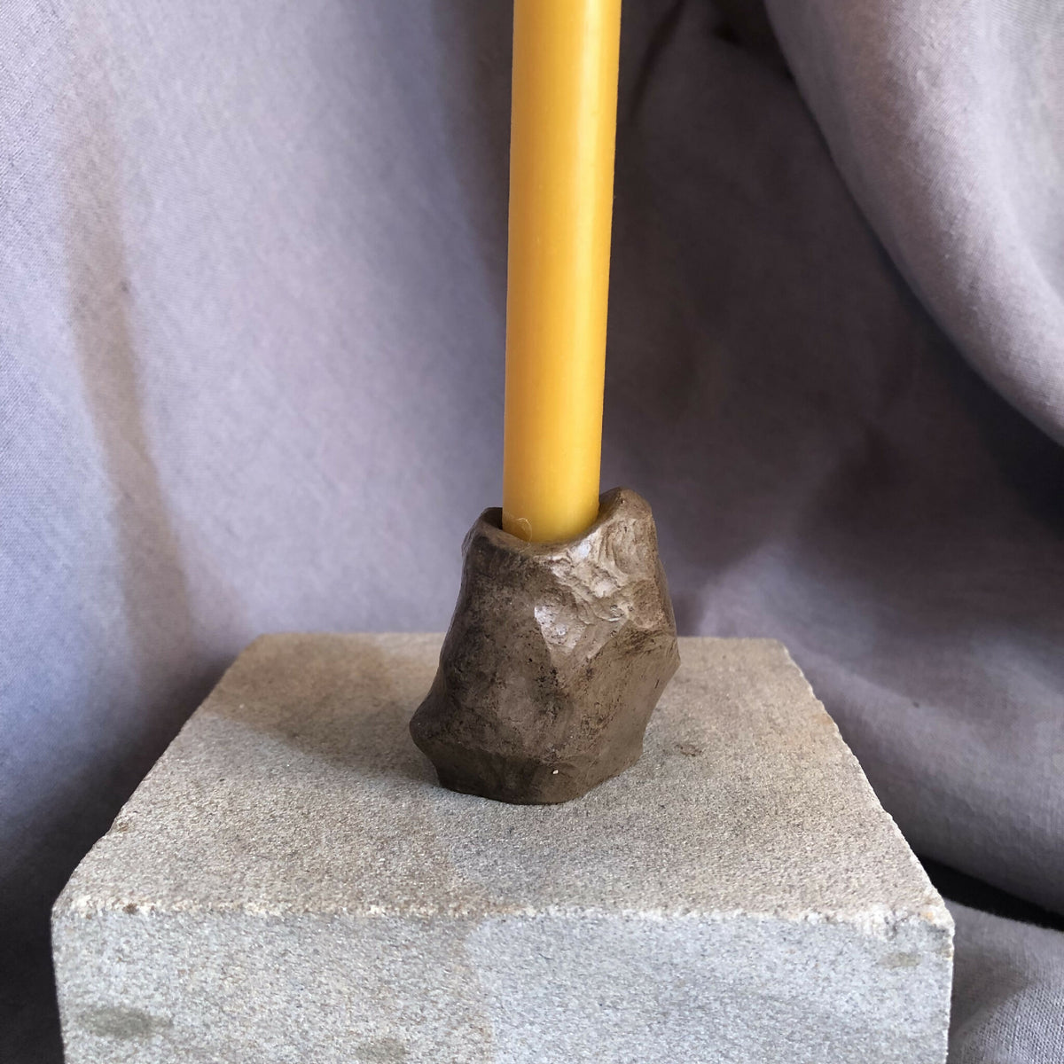 Mini bougeoir en pierre sombre et bougie jaune sur socle rectangulaire.