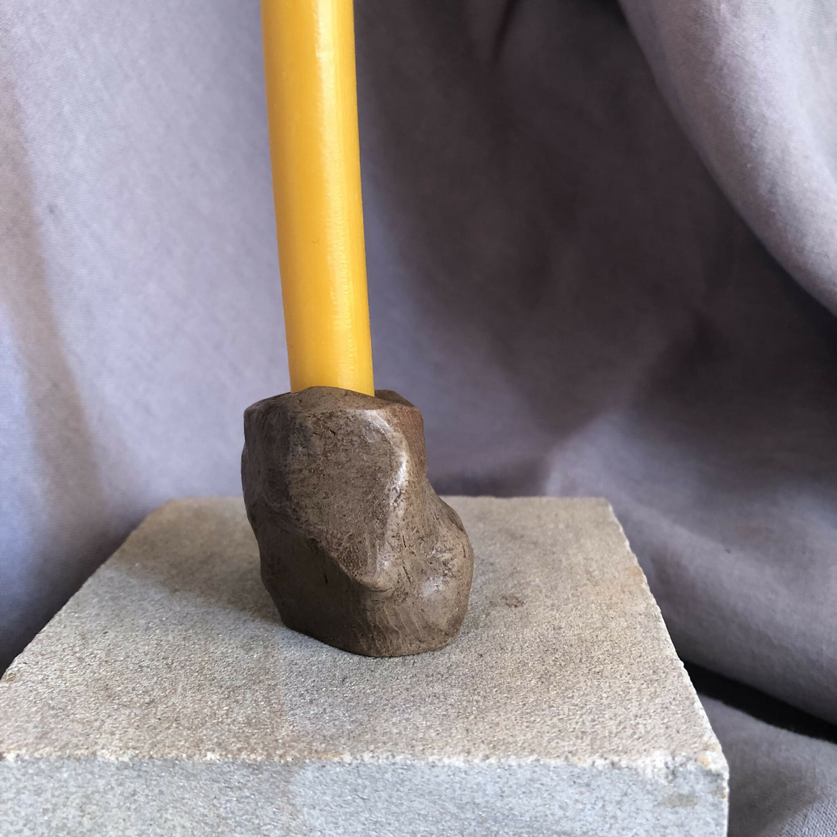 Mini bougeoir en pierre sombre avec bougie jaune, vue de dessus partielle.
