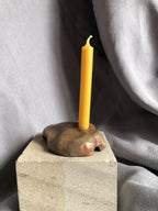 Mini bougeoir en pierre beige, bougie jaune allumée sur base carrée