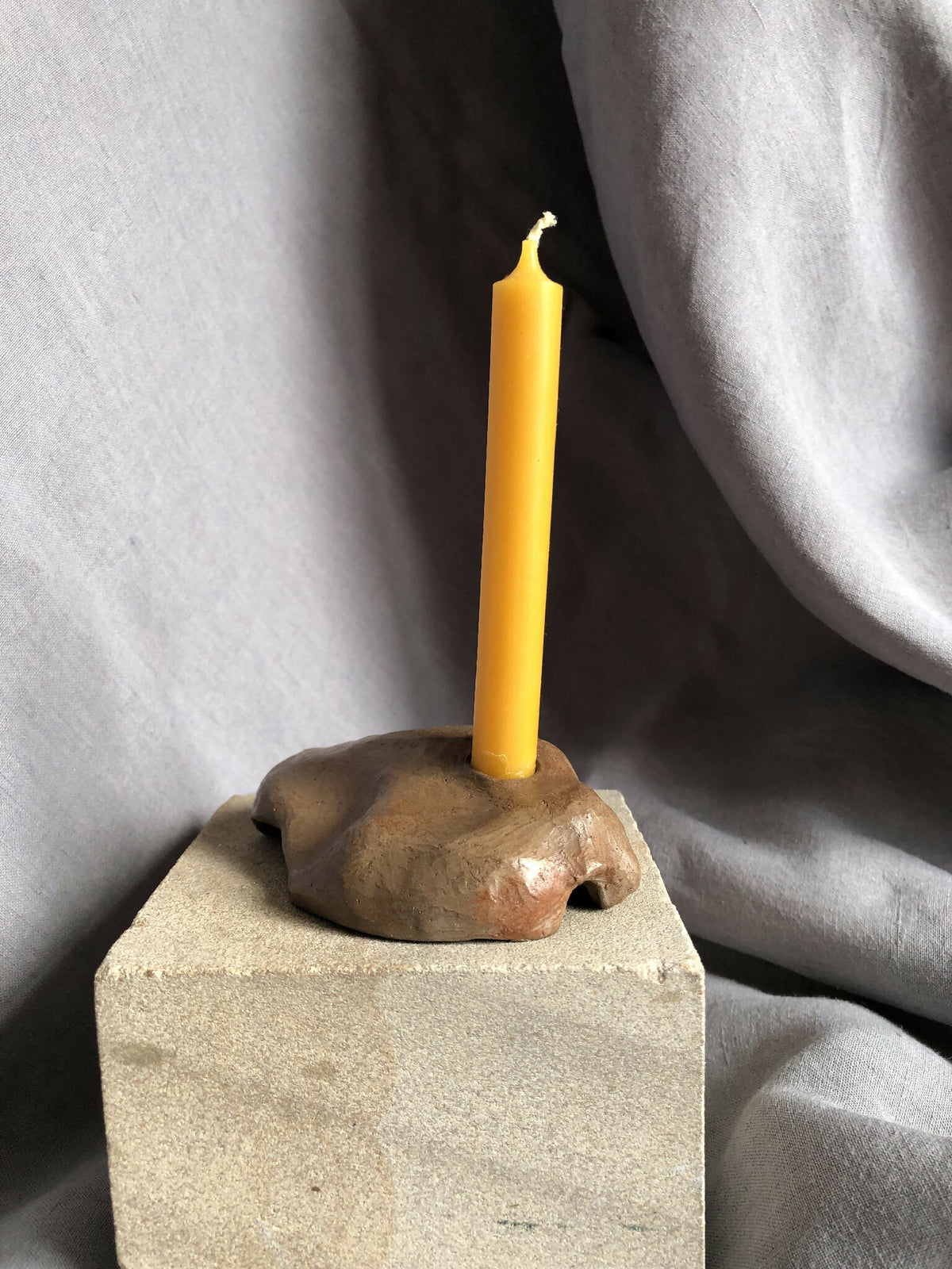Mini bougeoir en pierre beige, bougie jaune allumée sur base carrée