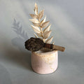 Petit pot en céramique rose pâle avec tige de feuilles dorées et fleur brune