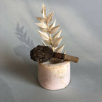 Petit pot en céramique rose pâle avec tige de feuilles dorées et fleur brune