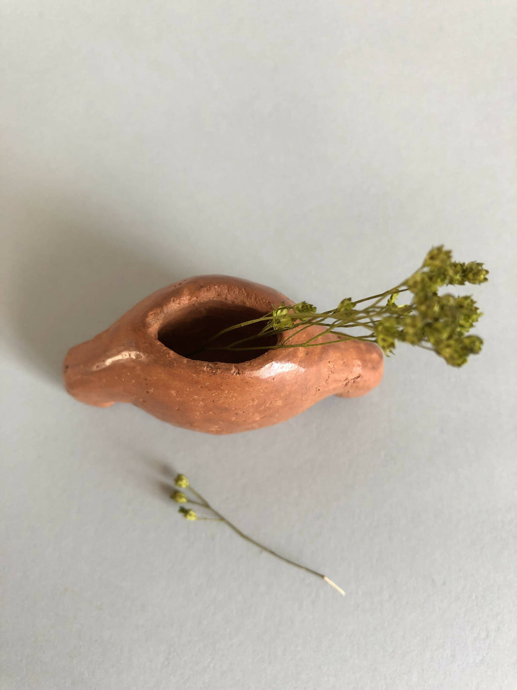 Petit vase en céramique brun cuivré avec ouverture ovale et plantes sèches.