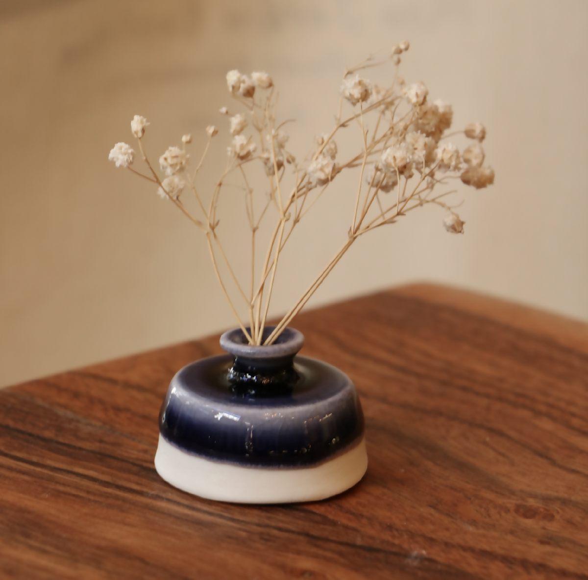 Mini-vase en porcelaine bleu nuit et base blanche, posé avec tiges fleuries séchées