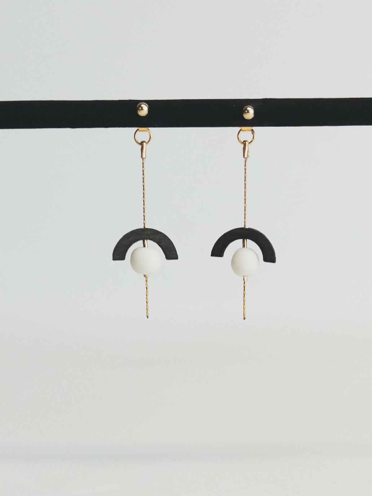 Boucles d’oreilles pendantes : demi-cercle noir, perle blanche, chaînette dorée.