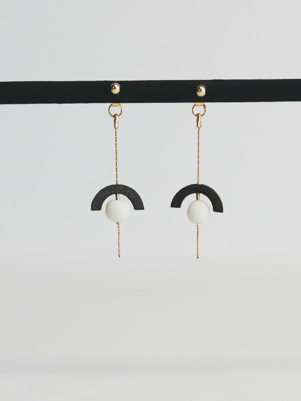 Boucles d’oreilles pendantes : demi-cercle noir, perle blanche, chaînette dorée.