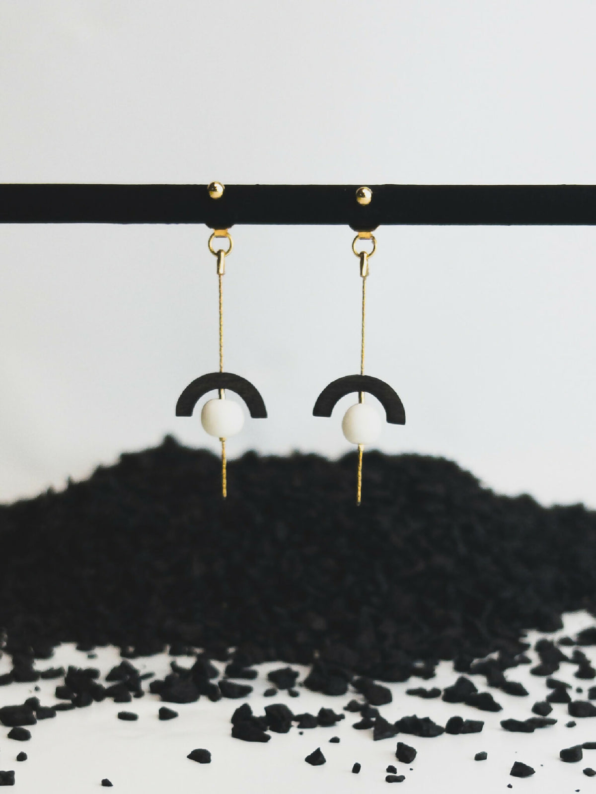 Boucles d’oreilles pendantes : crochet doré, demi-cercle noir et perle blanche.