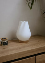 Lampe d’intérieur avec abat-jour blanc côtelé et base en bois sur une étagère.