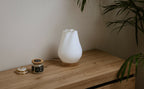 Lampe d’intérieur compacte à abat-jour blanc côtelé et base en bois, près d’objets.
