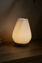 Lampe d’intérieur à abat-jour blanc côtelé avec base en bois, allumée.