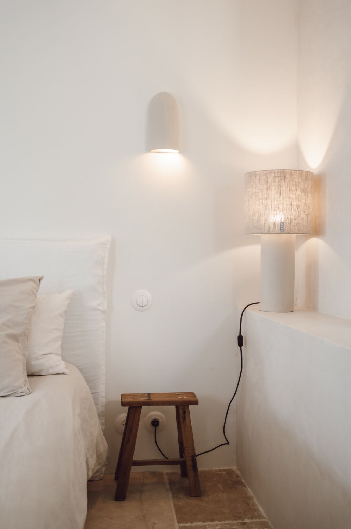 Lampe TERA allumée : abat-jour tissu beige sur base blanche, câble noir visible