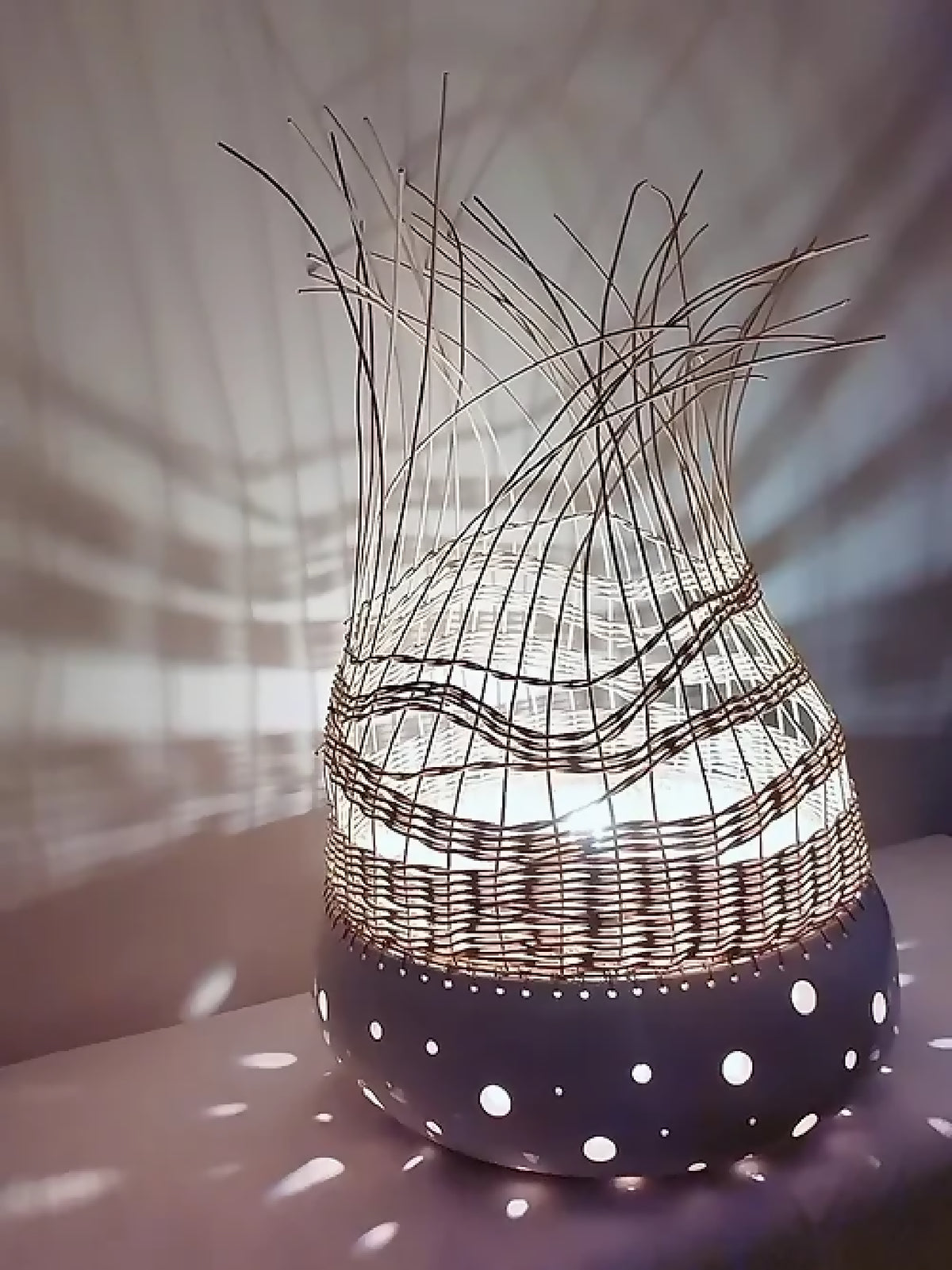 Lampe à poser tressée sombre sur base blanche à pois, fibres verticales au sommet.