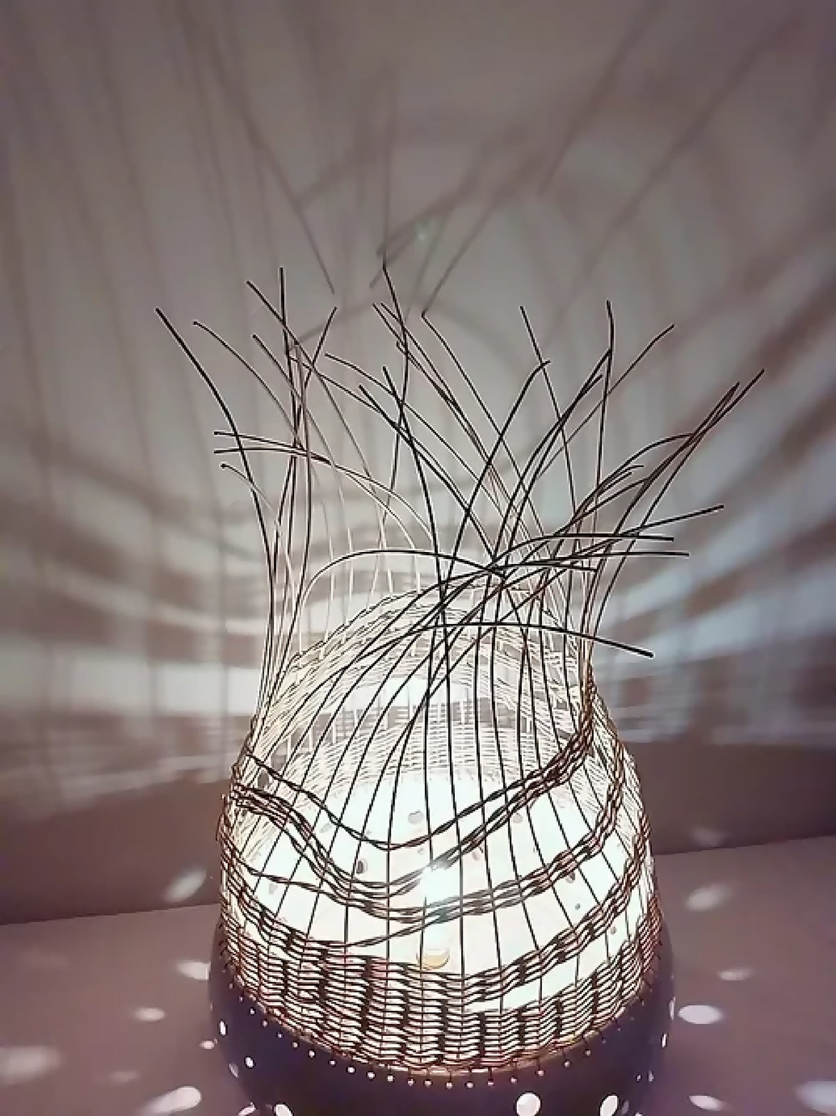 Lampe à poser en tressage sombre, base blanche à pois, fibres verticales au sommet.