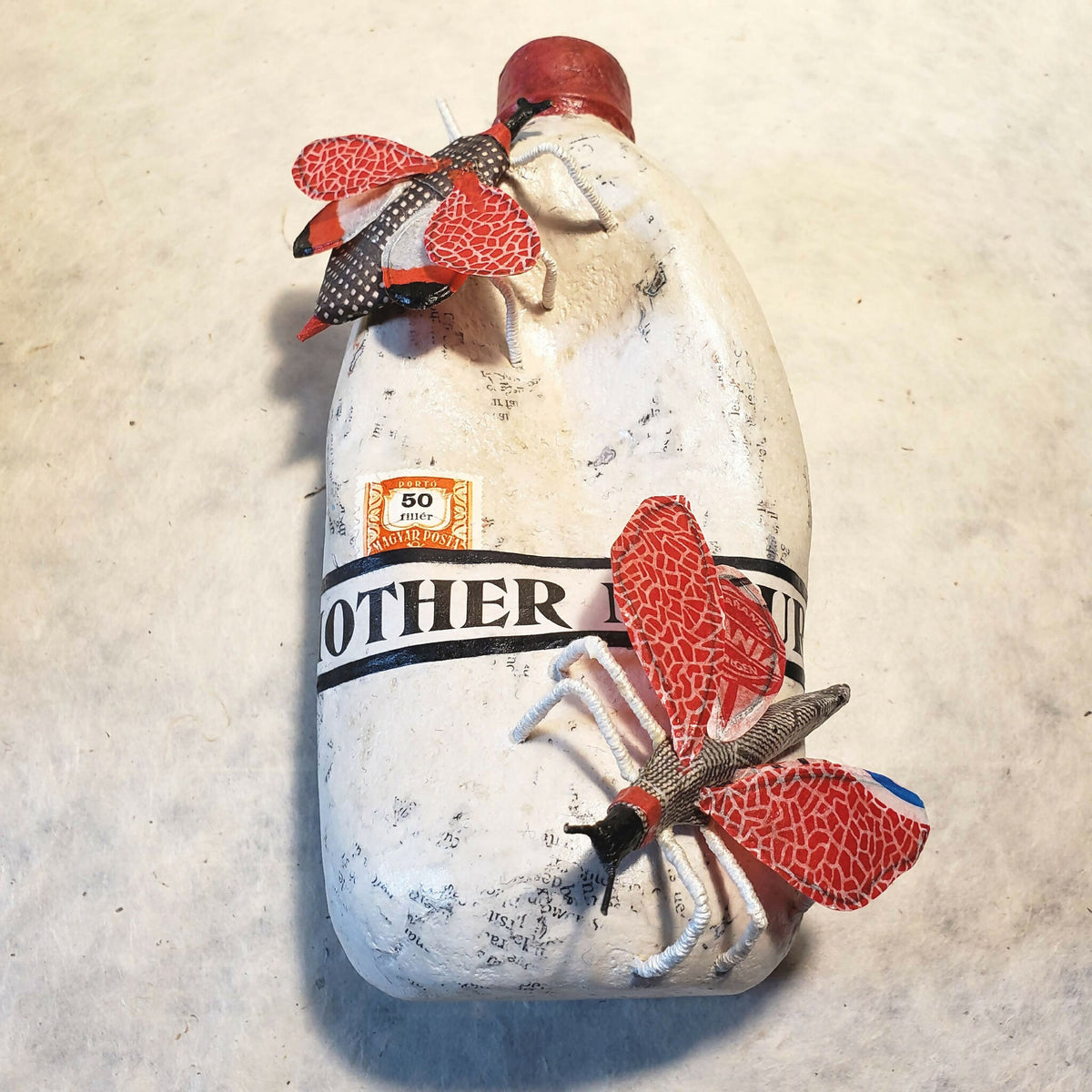 Sculpture de bouteille blanche avec chapeau rouge, papillons rouges et ruban noir