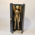 Sculpture papier de poupée beige aux ailes dorées, dans un écrin noir ouvert