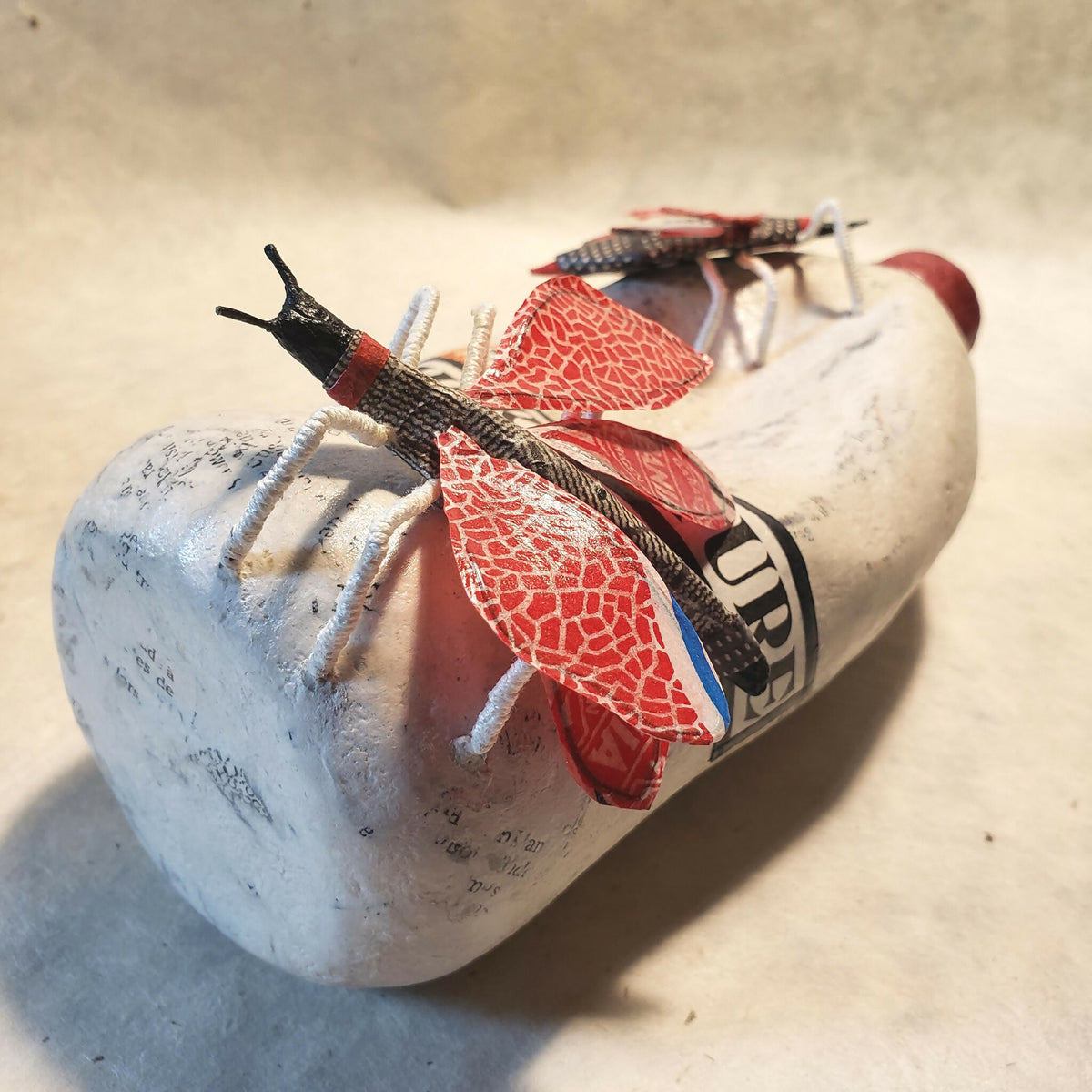 Sculpture de bouteille blanche vue de biais, chapeau rouge et papillons rouges