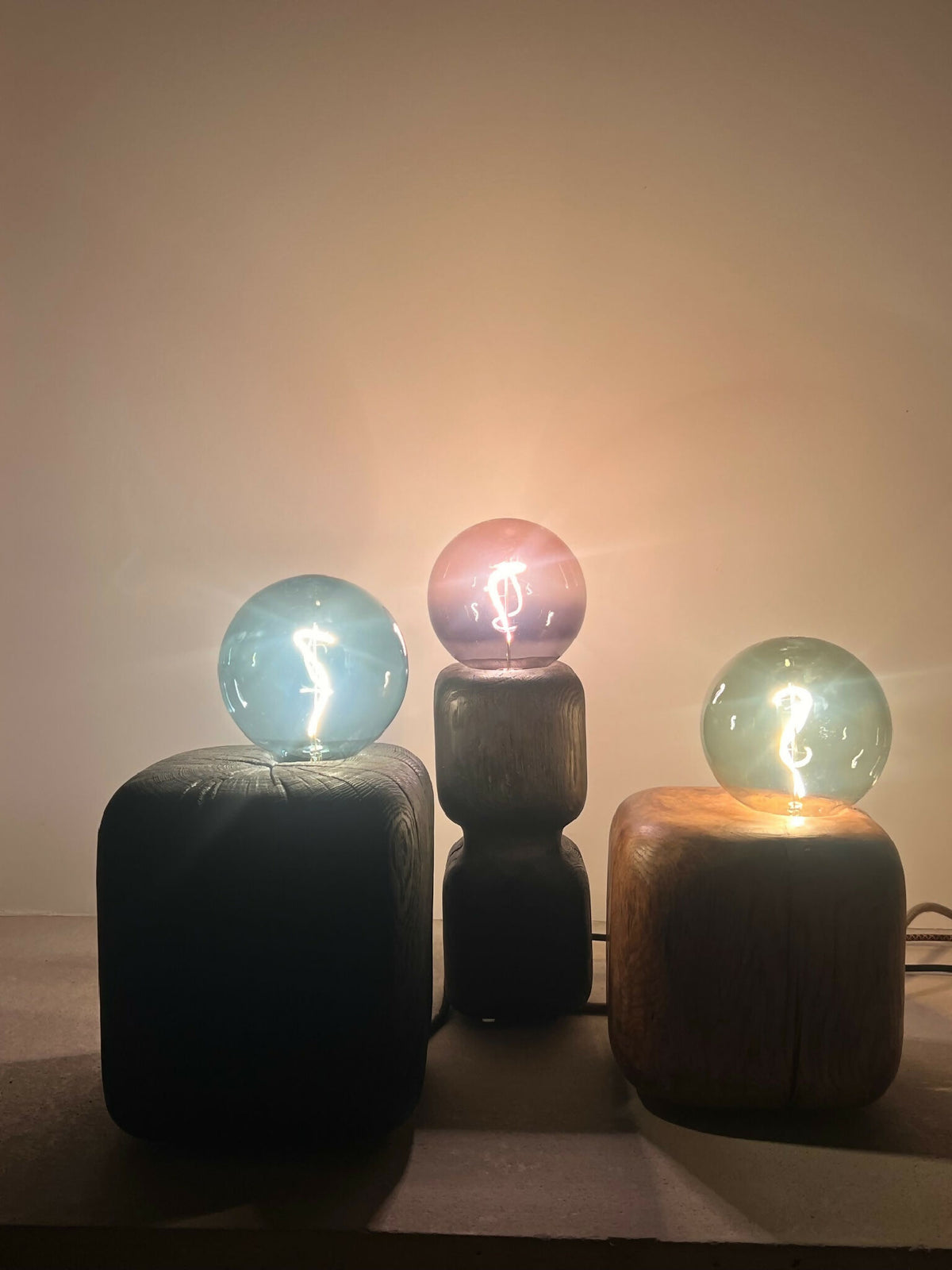 Ensemble de trois sculptures lumineuses : ampoules sphériques sur bases cubiques sombres.