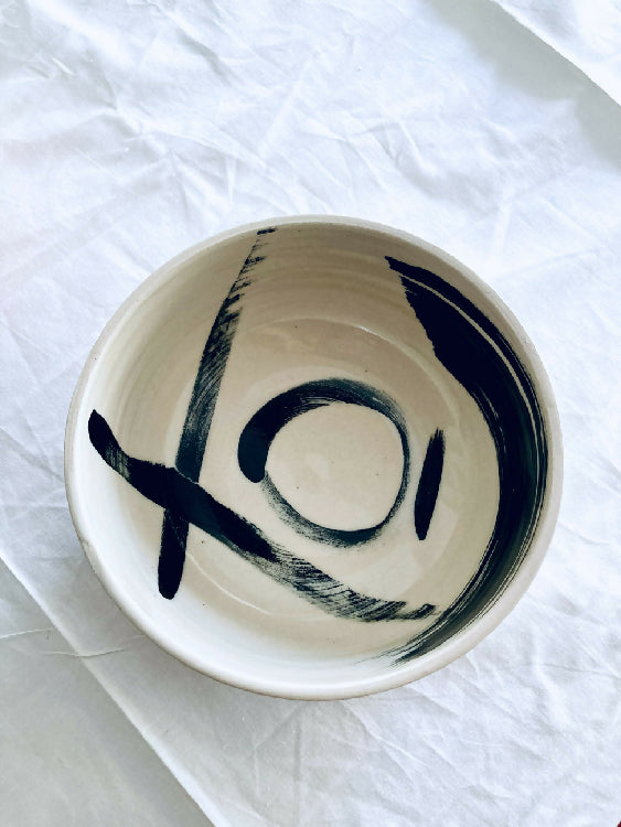 Bol en céramique beige avec grand motif noir stylisé sur le fond.