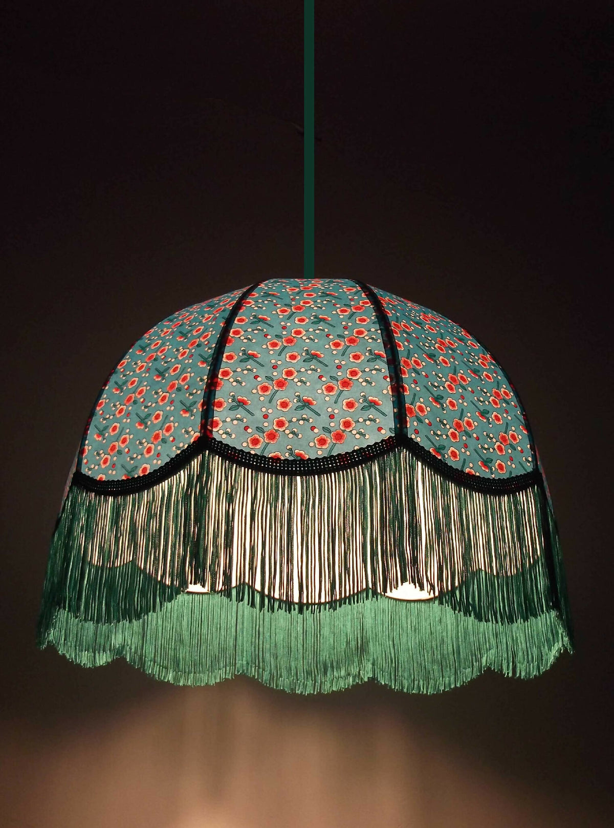 Suspension d’abat-jour bleu à fleurs, franges vertes longues et liserés noirs.