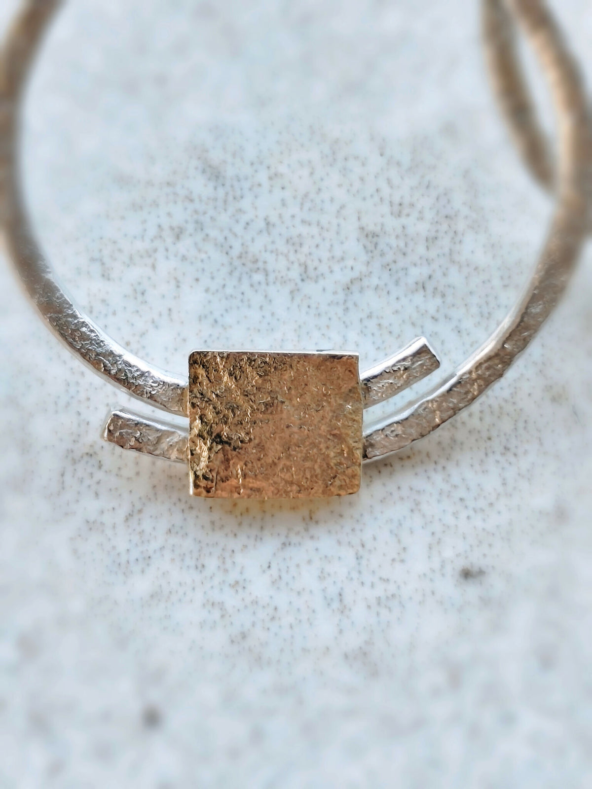 Détail d’une boucle d’oreille créole argentée avec grande pastille carrée dorée