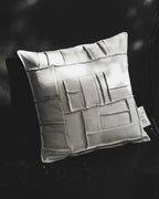 Coussin carré ivoire à reliefs géométriques façon briques, coutures décoratives.