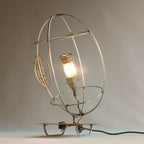 Lampe RUGBY allumée : cage ronde dorée, ampoule éclairante et base sur pied