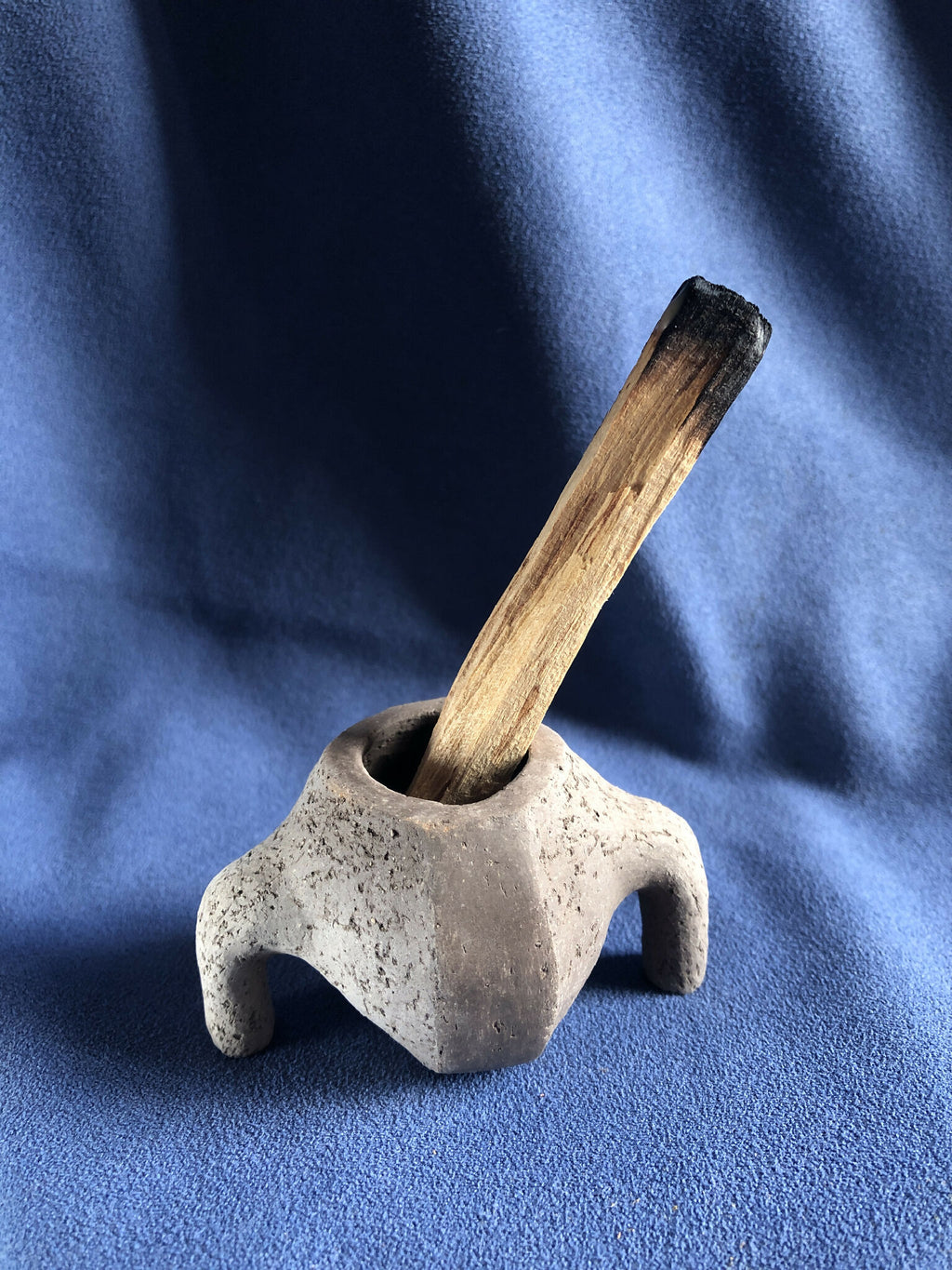 Petit pot en pierre gris clair avec tige en bois foncée dans l’ouverture.