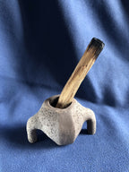 Petit pot en pierre gris clair avec tige en bois foncée dans l’ouverture.