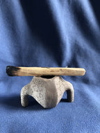 Petit pot en pierre grise avec branche en bois posée au-dessus de l’ouverture.