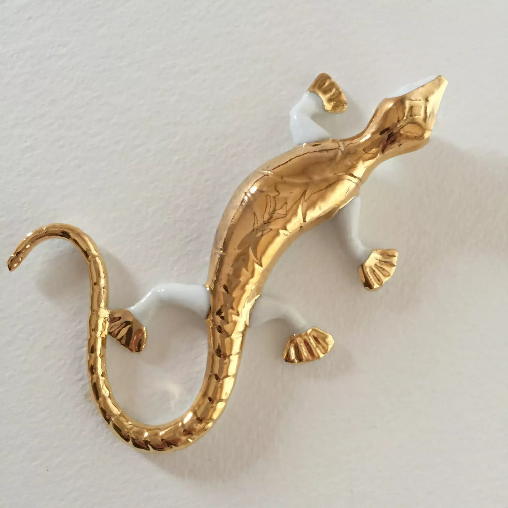 Sculpture de salamandre dorée sur fond clair, queue en boucle et détail des pattes