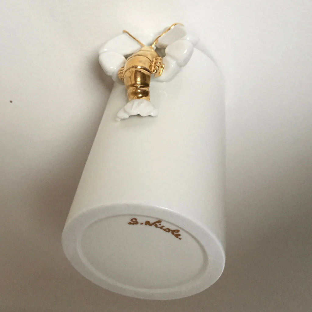 Vase homard blanc avec figurine dorée, vue du fond avec inscription.