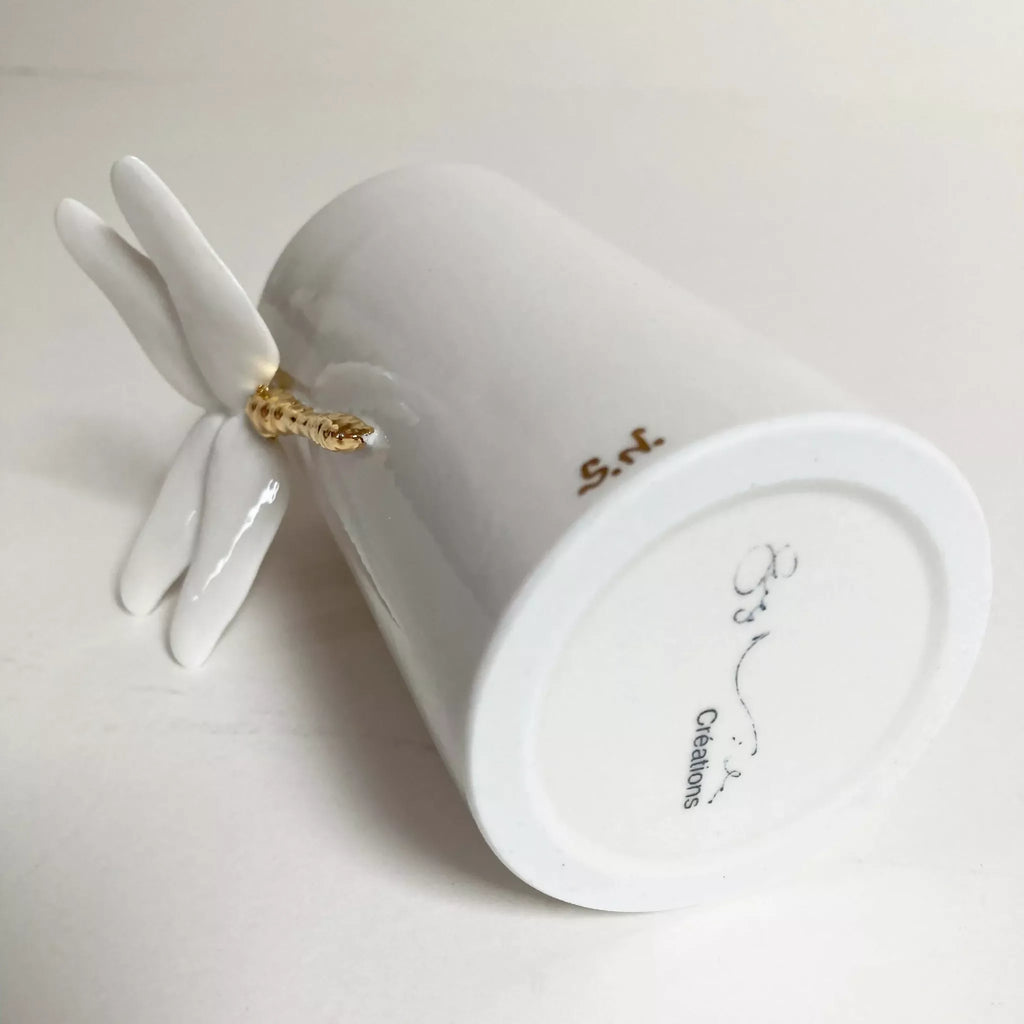 Vase blanc, base circulaire avec inscription, libellule dorée sur une aile.