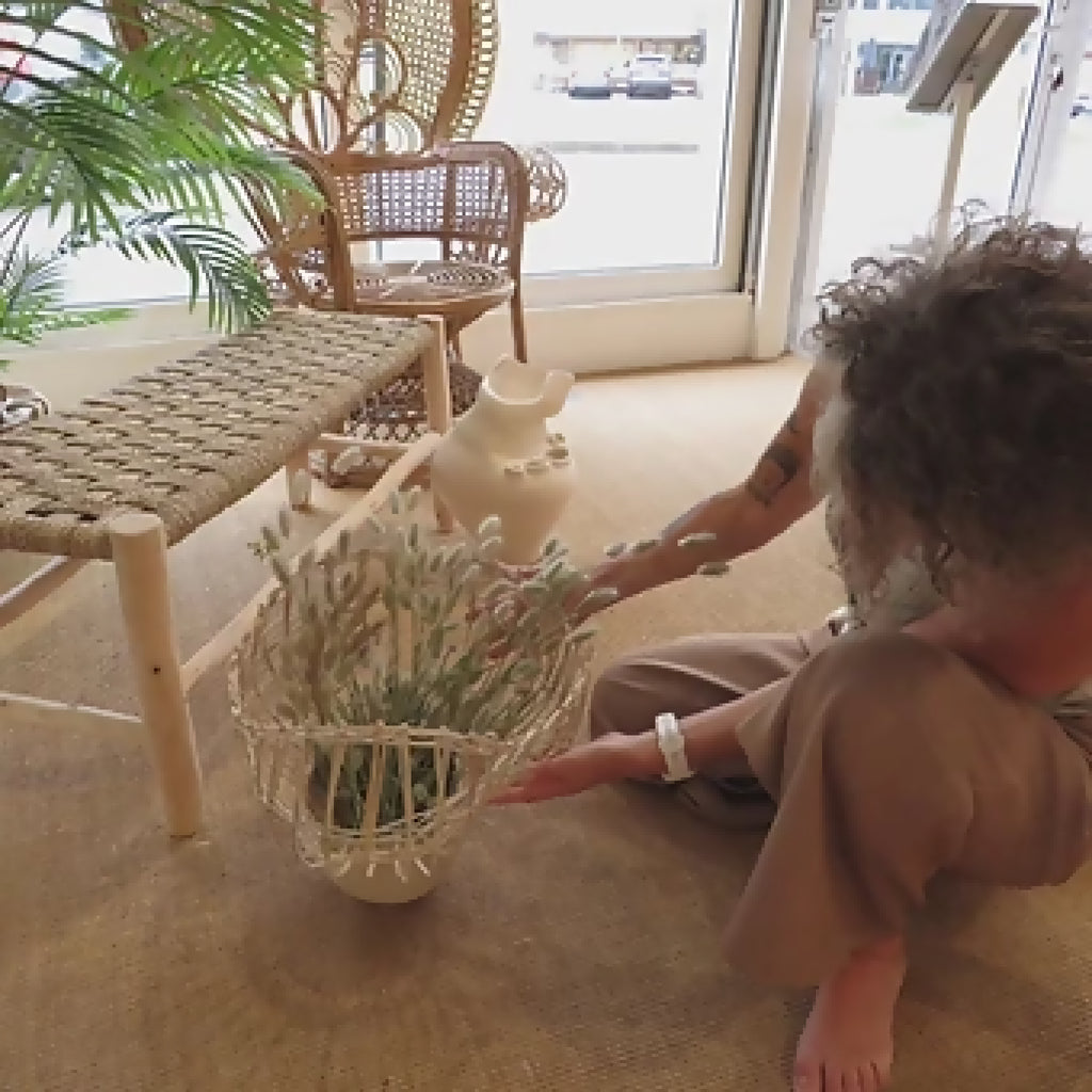 Vase en céramique beige avec décor de fibres et herbes, posé au sol