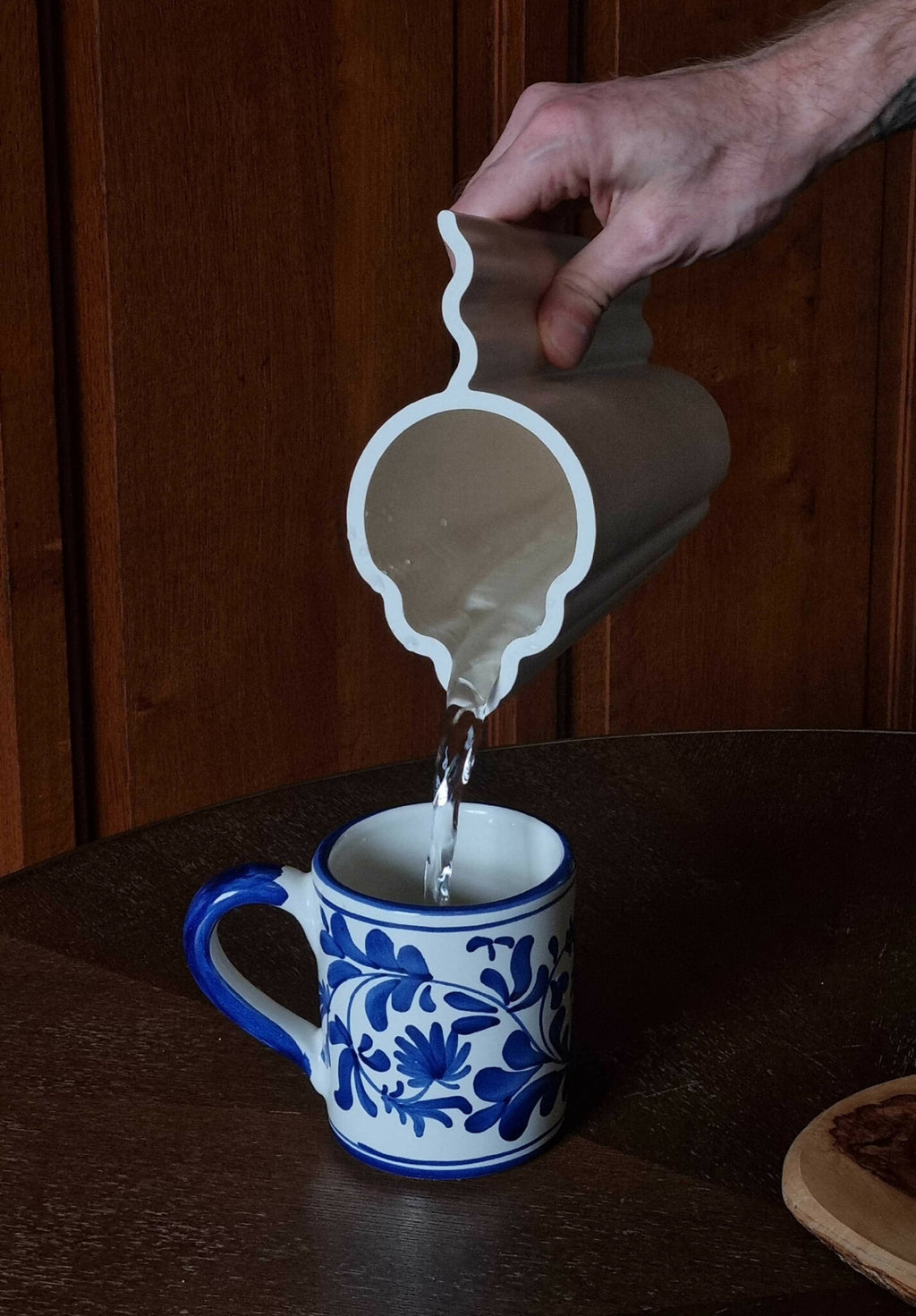 Vase blanc tenu à la main, versement d’un liquide dans une petite tasse bleue.