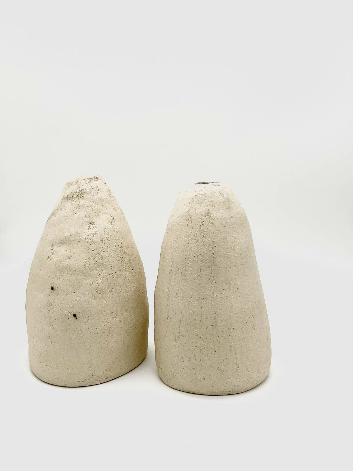 Deux vases coniques DUO beige, texture granuleuse et ouvertures noires en haut.