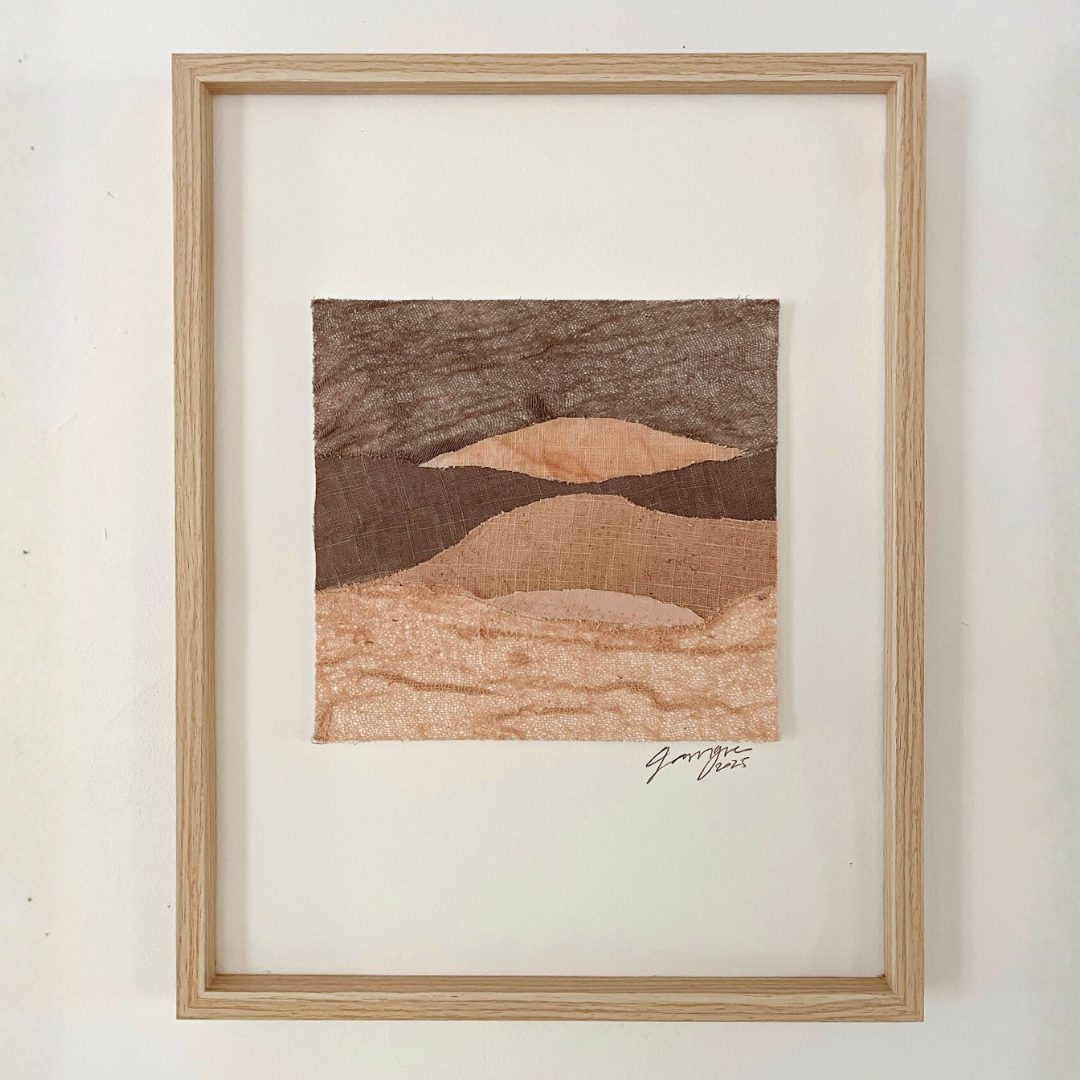 Collage textile encadré en bois clair, paysage abstrait de collines aux tons bruns et beiges.