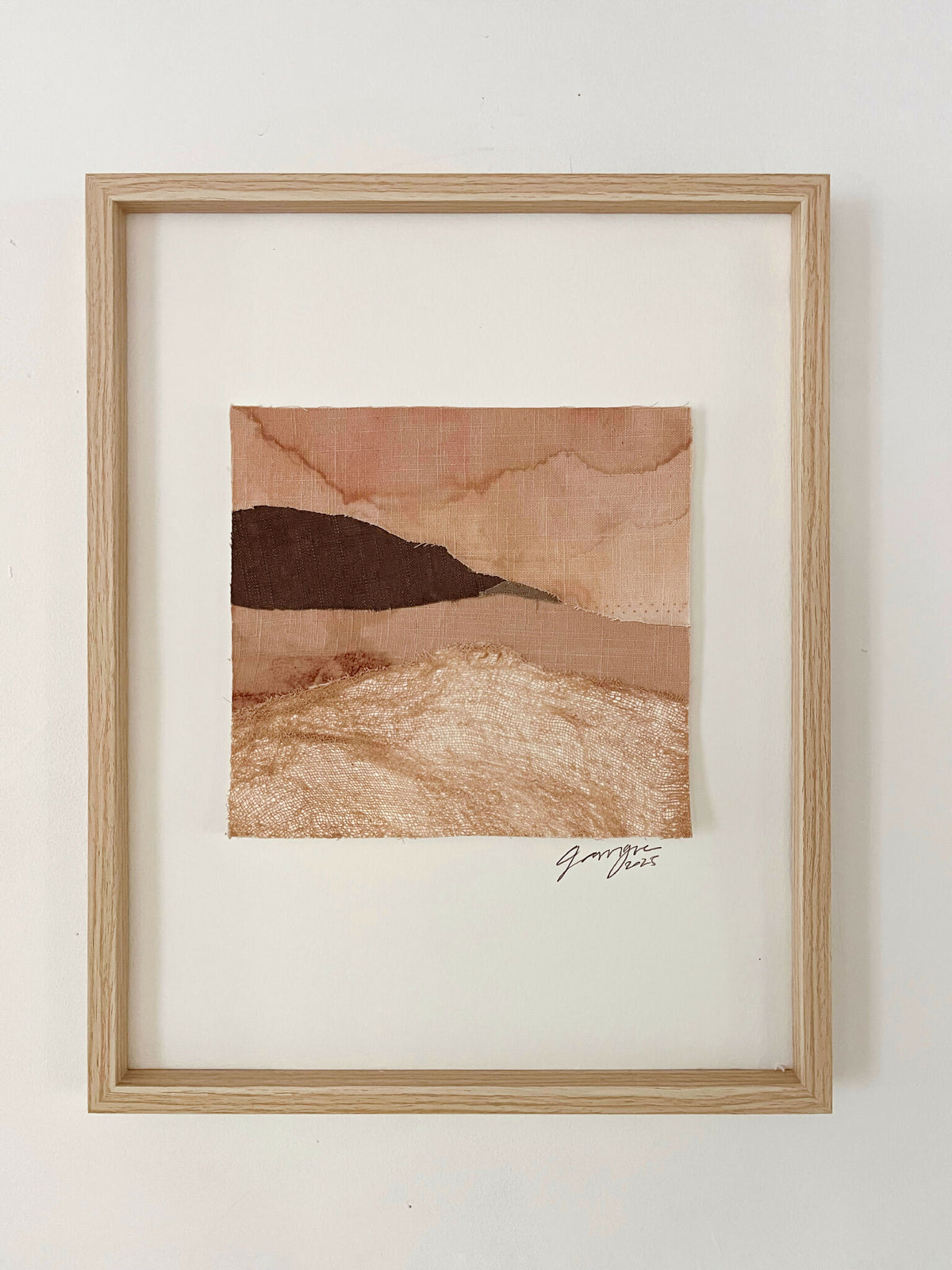 Collage textile encadré, paysage superposé beige et brun, signature en bas à droite.