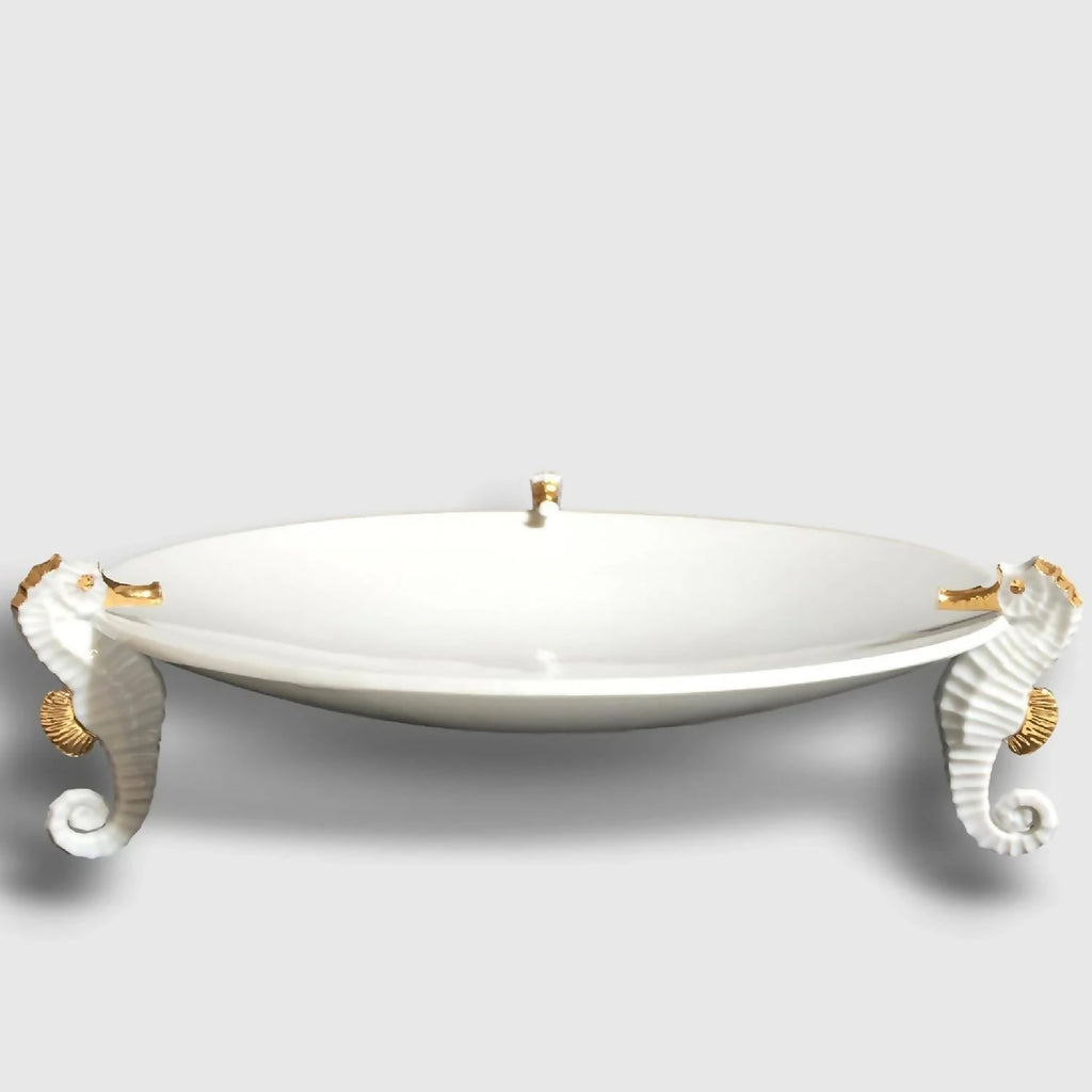 Centre de table hippocampe : plat blanc sur quatre figurines d’hippocampes dorées et grises.