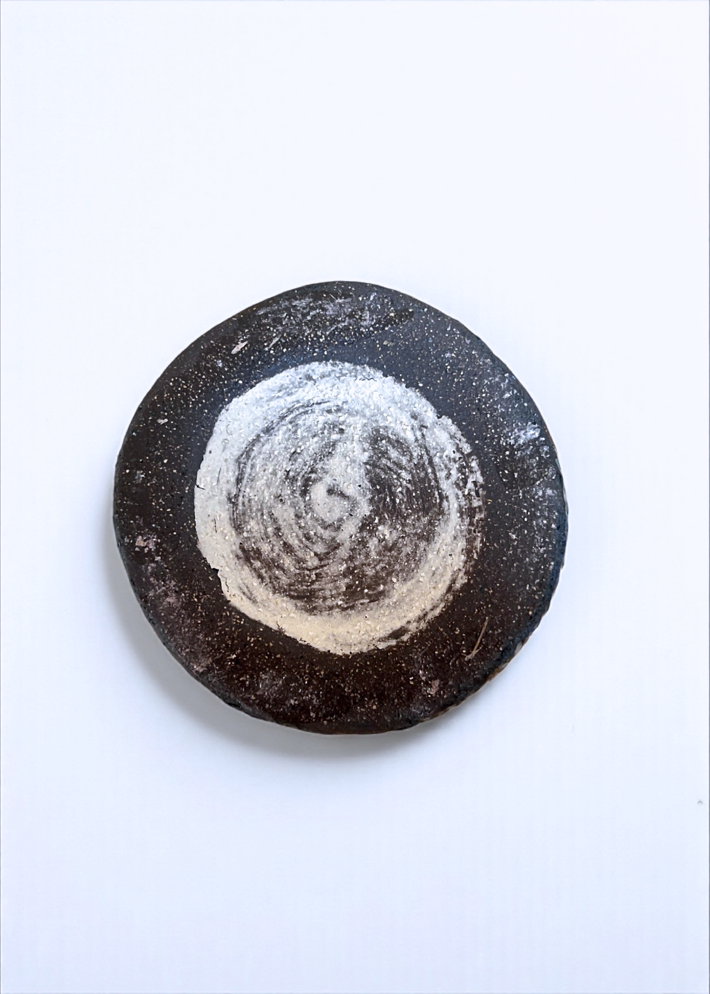 Dessous d’un petit vase en grès : surface sombre striée avec cercle clair