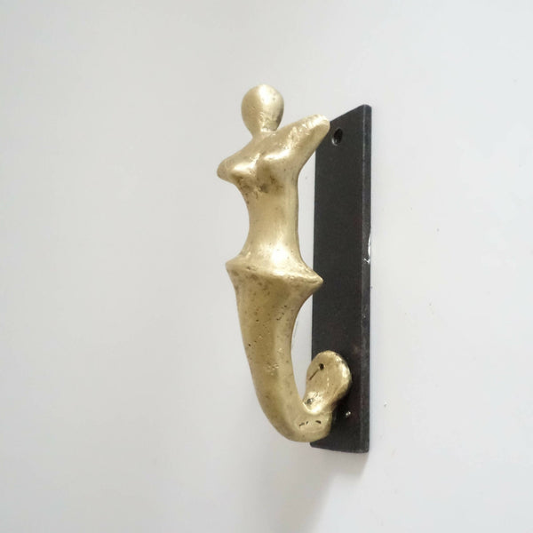 Porte-manteau mural avec patère en forme de figurine dorée sur plaque noire.