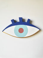 Œil en peinture sur bois, fond blanc, iris bleu clair et pupille orange.