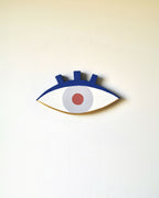 Petit œil en bois peint, contour bleu foncé, iris bleu clair et pupille orange.