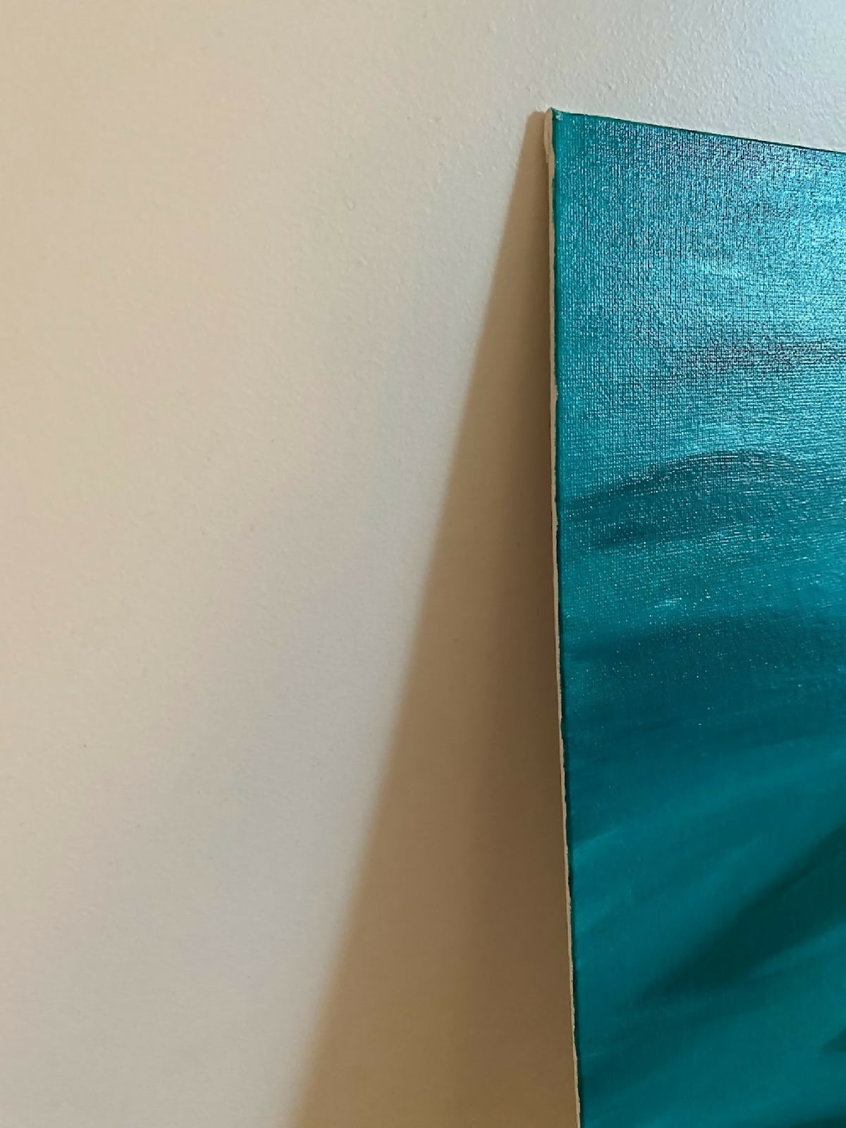 Coin de toile abstraite bleu-vert sur mur, bord de toile et coups de pinceau.