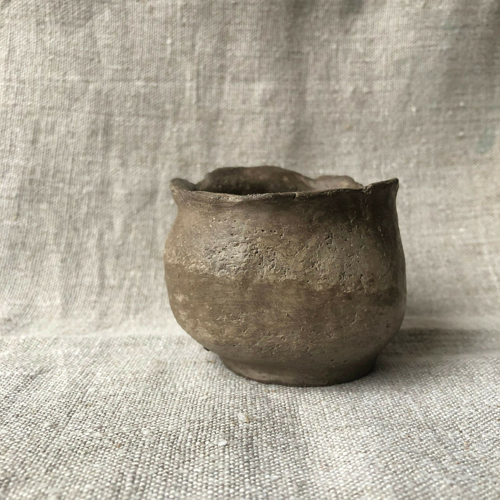 Petit pot en terre cuite gris foncé, forme trapue arrondie, intérieur sombre.