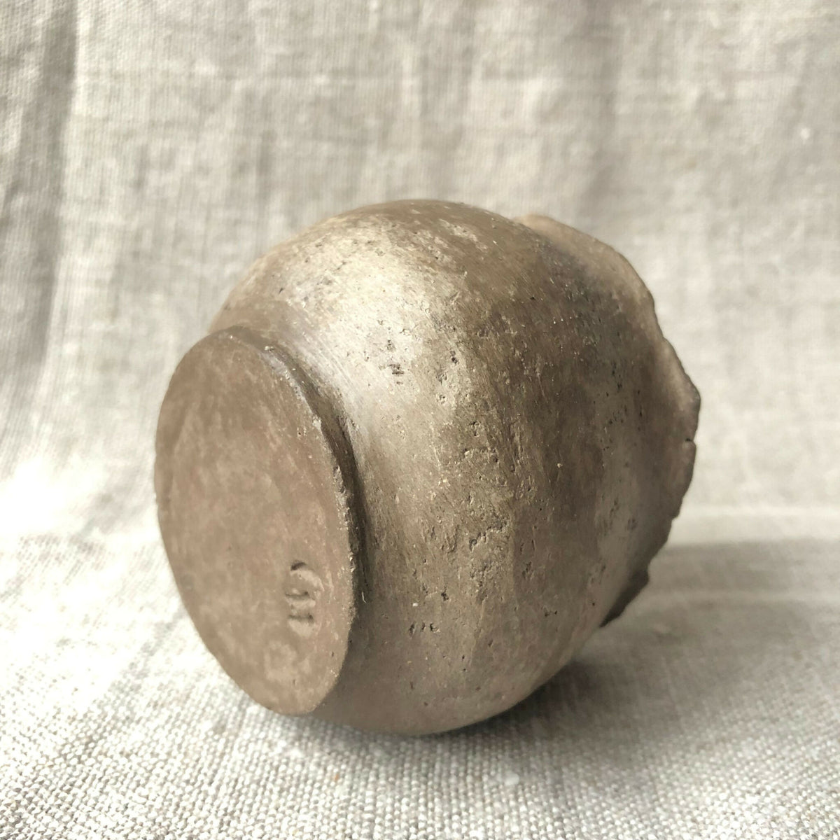 Petit pot en terre cuite patinée gris clair, vue de côté, surface granuleuse.